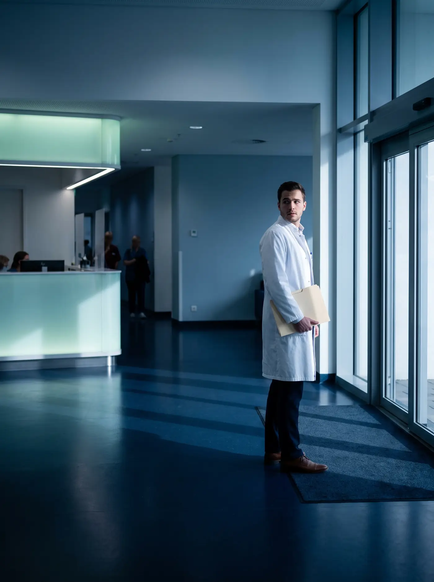 Jovem médico de jaleco, com uma pasta na mão, na recepção de um hospital